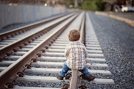 depth of field photography of boy sitting on brown metal train railway thumbnail