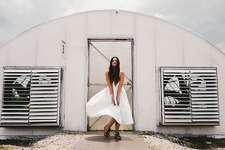 woman wearing white sleeveless dress standing in front of white painted door thumbnail