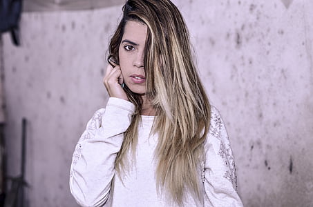 woman standing near white wall while right hand holding hair thumbnail