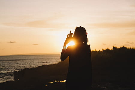 Silhouette of Woman Standing Near Body of Water during Sunset thumbnail