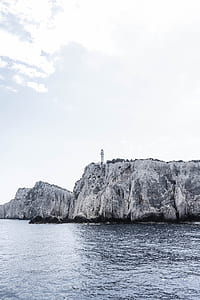 white lighthouse at the cliff near body of water under white skies thumbnail