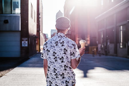 person wearing gray and black shirt holding ice cream standing on the road near buildings during daytime photography thumbnail