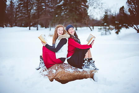 two women sitting on brown rock covered with snow thumbnail