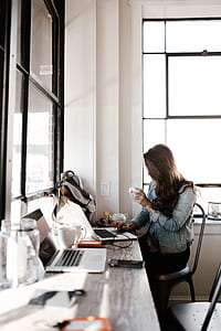 woman holding white ceramic cup while working on laptop thumbnail