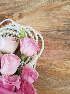 pink roses and beaded white pearl necklace on brown wooden board thumbnail