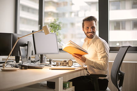 A young man smiling while holding notebook in his hands at his workstation thumbnail