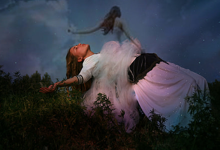 woman in white elbow sleeved long dress bending surrounded with plants thumbnail