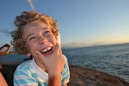 photo of boy wearing white and blue striped collared top standing on rock formation during sunset thumbnail