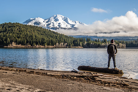 man standing on log near mountain at daytime thumbnail