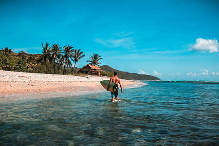 man carrying a green surfboard walking on seashore thumbnail