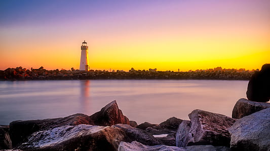 white lighthouse near body of water during orange sunset thumbnail