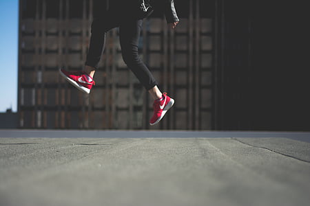 person wearing red Nike sneakers jumping on road during day thumbnail