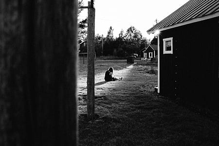 grayscale photography of woman sitting on grass near the house thumbnail