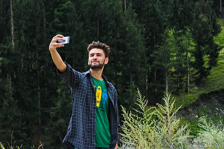 Man in Blue Sports Shirt and Green Top Taking a Selfie Near Green Trees thumbnail