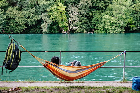 person lying on hammock beside body of water during daytime thumbnail