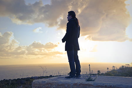 A caucasian man with long hair standing on a seashore at sunset thumbnail