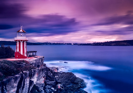 red and white lighthouse near body of water under cloudy sky thumbnail