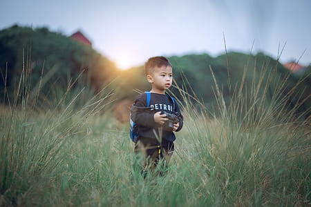 Shallow Focus Photography of Boy Standing on Green Grass Holding Camera thumbnail