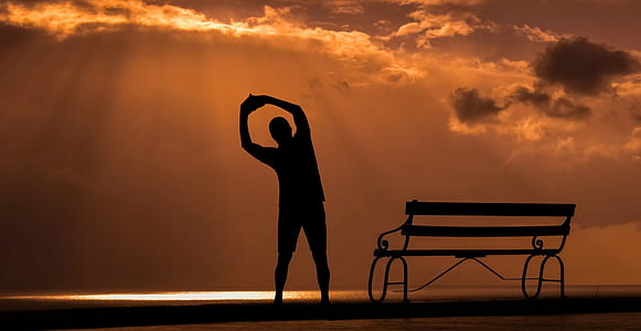 silhouette of stretching man beside bench during golden hour thumbnail