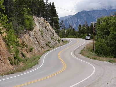 black vehicle parked beside road and cliff with trees at daytime thumbnail