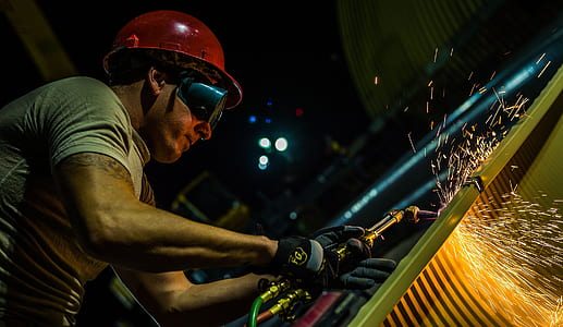 man wearing black goggles and red hard hat welding metal thumbnail