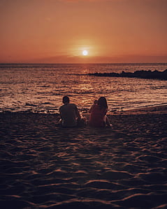 couple sitting on beach sand facing golden hour thumbnail