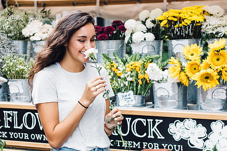 woman smelling white carnation flower while walking beside yellow sunflowers and white chrysanthemums display thumbnail