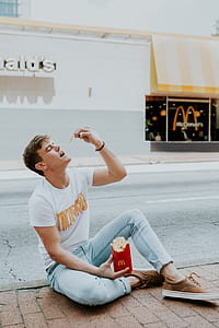 man holding McDonald fries sitting on brown and gray concrete pavement thumbnail
