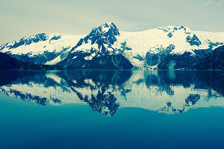 black mountain covered with snow and body of water thumbnail