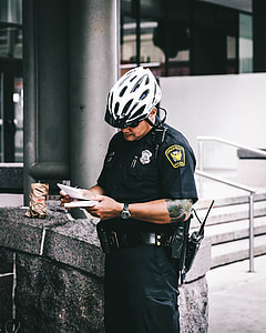 Policeman holding white notepad and black pen standing near gray concrete bench outside building thumbnail