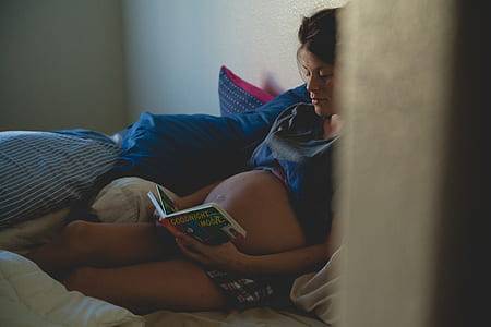pregnant woman leaning on wall reading book while on bed thumbnail
