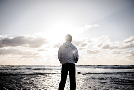 gray scale photo of man wearing jacket facing body of water at daytime thumbnail