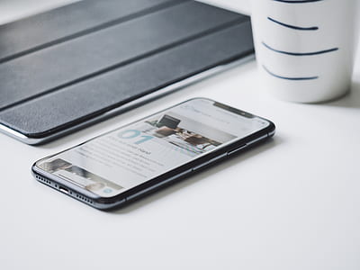 black smartphone on white board beside cup thumbnail