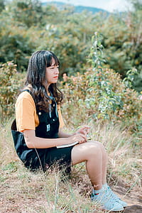 Photo of Woman Sitting on Ground Surrounded by Grass, Trees, and Plants thumbnail