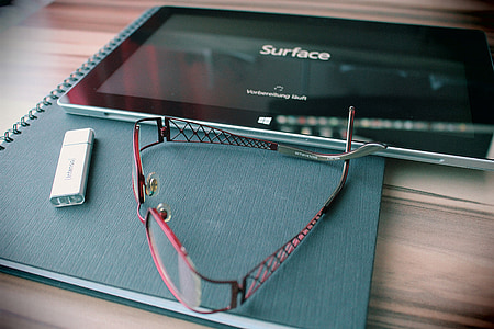 red framed eyeglasses near black Microsoft Surface Pro on top of table thumbnail