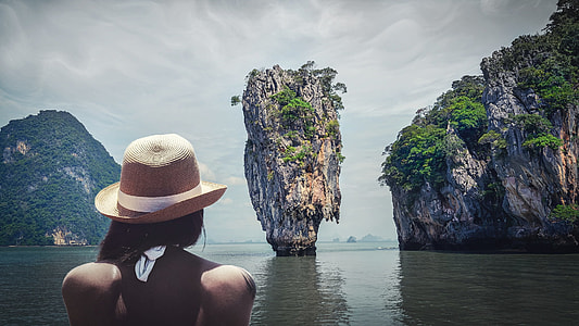 woman wearing beige sun hat starring at cliff in the middle of water during day time thumbnail