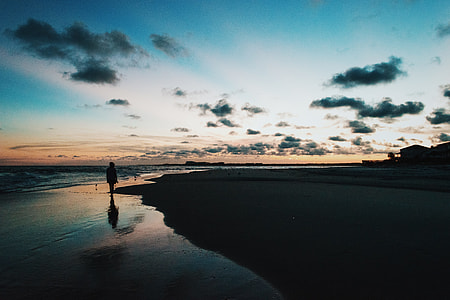 silhouette of person standing on seashore at dusk thumbnail