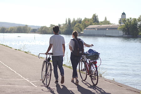 couple walking and holding bicycle beside body of water thumbnail