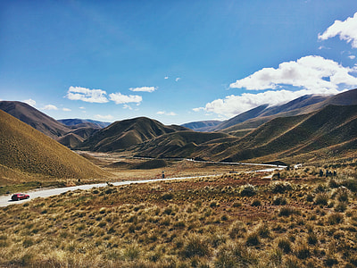 red SUV on road near brown mountains under white clouds during daytime thumbnail
