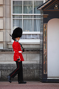 man in black and red suit holding rifle walking beside gray concrete building at daytime thumbnail
