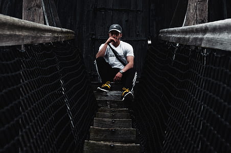 man in white T-shirt sitting on hanging bridge during daytime thumbnail