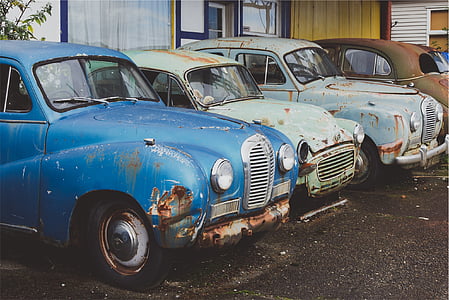 several blue, white, and brown vehicles parked on row behind white painted wall thumbnail
