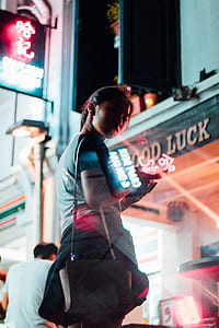 woman in blue top wearing sling bag and using smartphone in front of store thumbnail