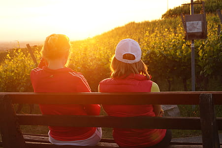 two women sitting on wooden bench facing the sunlight thumbnail
