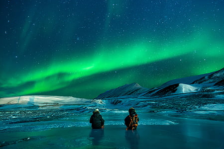 two people partially submerged on water surrounded by snow overlooking aurora borealis thumbnail