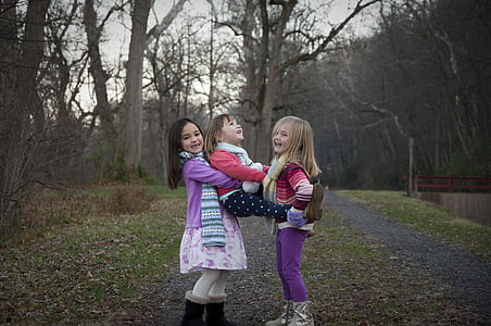 three girls playing near trees during daytime thumbnail
