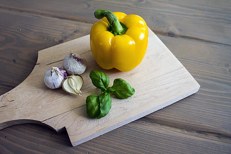 yellow bell pepper and garlic, onion and green vegetable leaves on top of chopping board thumbnail