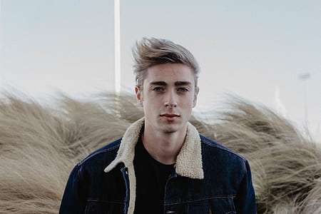 man wearing blue denim jacket behind wheat grass thumbnail