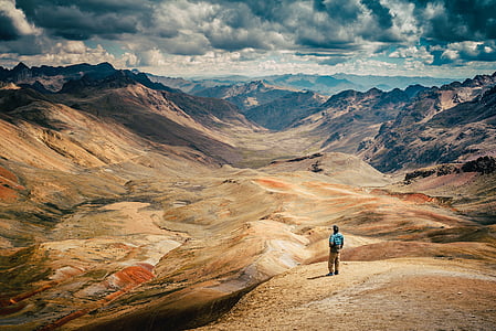 man standing on the cliff facing the rocky mountain during daytime thumbnail
