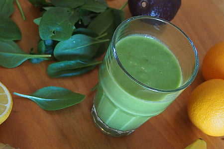 cup of smoothie beside yellow citrus and green leaves all on top of brown wood surface thumbnail